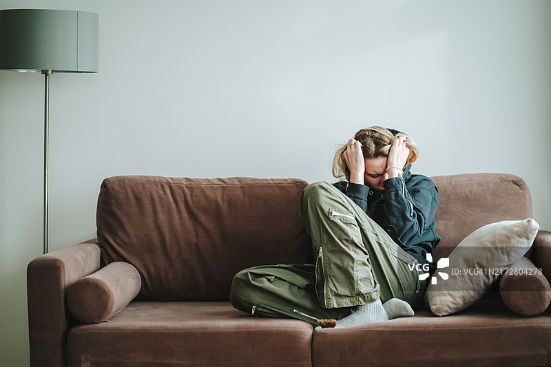 分手后的孤独和沮丧：在沙发上用手捂着头哭泣的女人图片素材