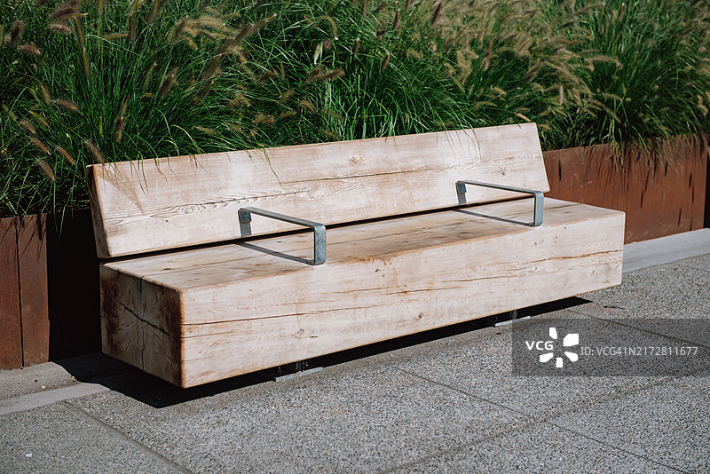 阳光明媚的城市公园里带钢制扶手和花坛的现代木制长椅图片素材