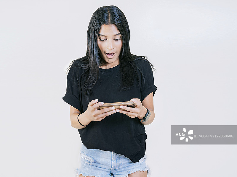 快乐的少女正在使用并看手机，一个快乐的年轻女孩看着手机上的促销活动图片素材