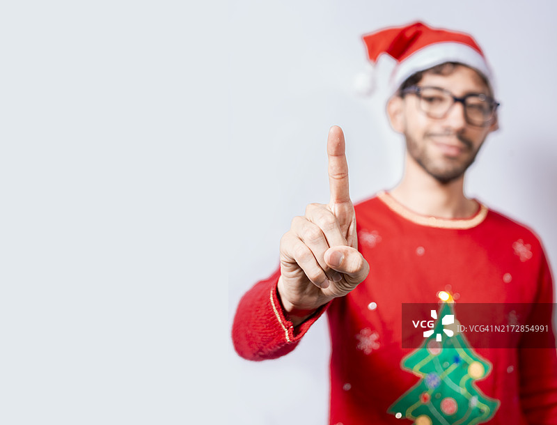 戴着圣诞帽的男子用手指比划数字一。穿着圣诞服装的男子用手指比划数字一。穿着圣诞服装的男子比划数字一的概念图片素材
