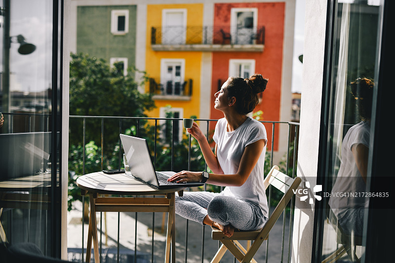 在西班牙阳台上用笔记本电脑工作的女数字营销员图片素材