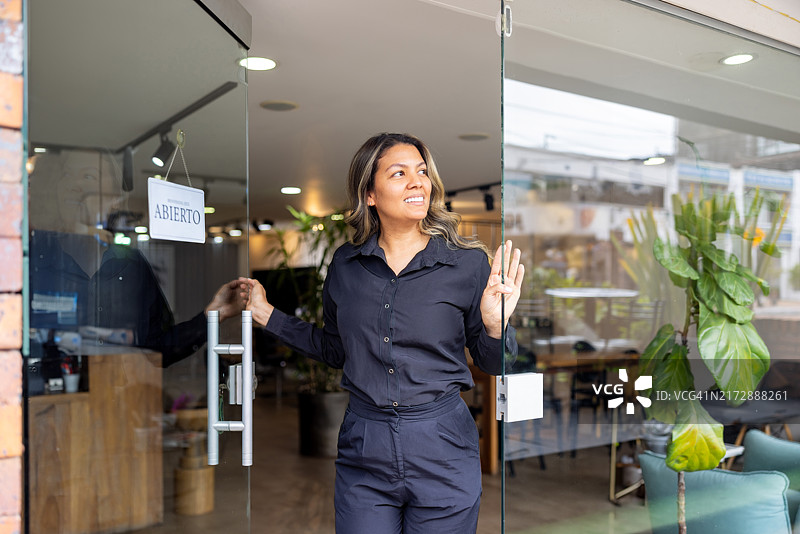 理发师打开她的美发沙龙的门并看向别处图片素材
