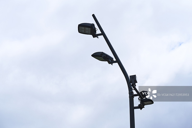 白天多云天空背景下的金属灯杆低角度视图图片素材