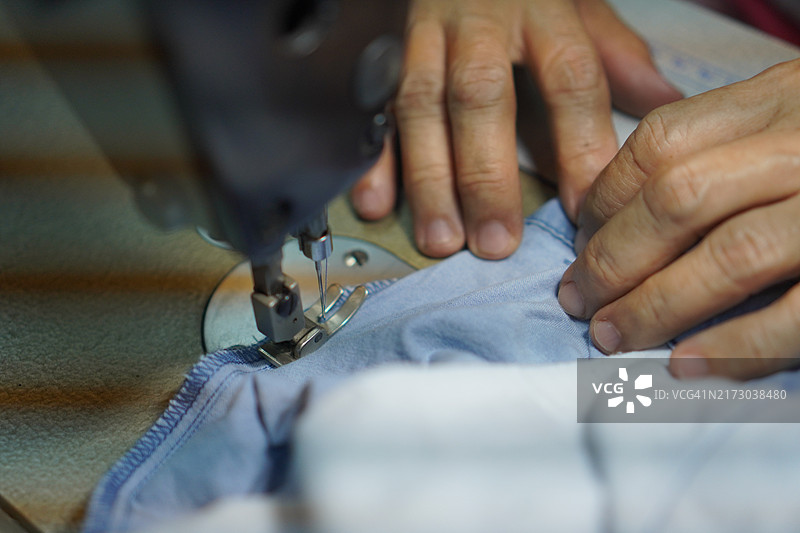 女人的手在缝纫机上操作配件设备，白色织物特写图片素材