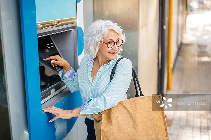年长的女人在西班牙巴塞罗那的ATM机上用信用卡取款图片素材