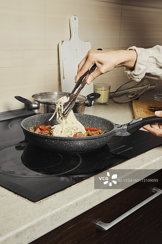 将煮熟的米粉和蔬菜调料、牛肉一起放入煎锅中的匿名女子图片素材