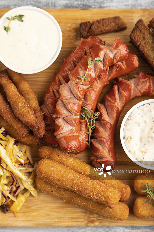 小吃合集：香肠、鸡块、奶酪条、吐司、卷心菜沙拉，灰色木质背景。俯视、平铺、特写图片素材
