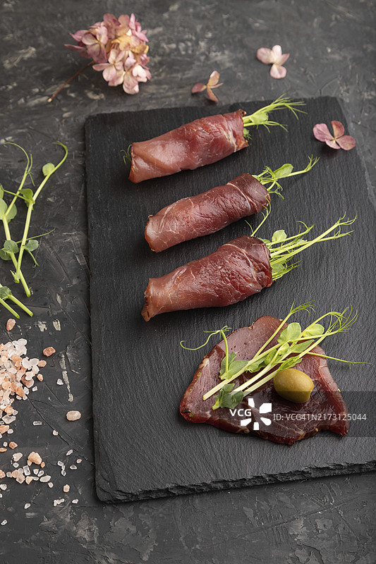 烟熏腌肉片配绿色豌豆苗，黑色混凝土背景。图片素材