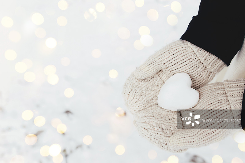 戴手套的女孩手中的雪心雪球。模糊背景图片素材