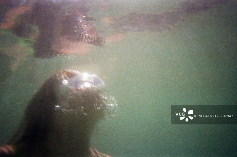 一个人游向水面吹泡泡的水下拍摄，使用一次性水下相机拍摄图片素材