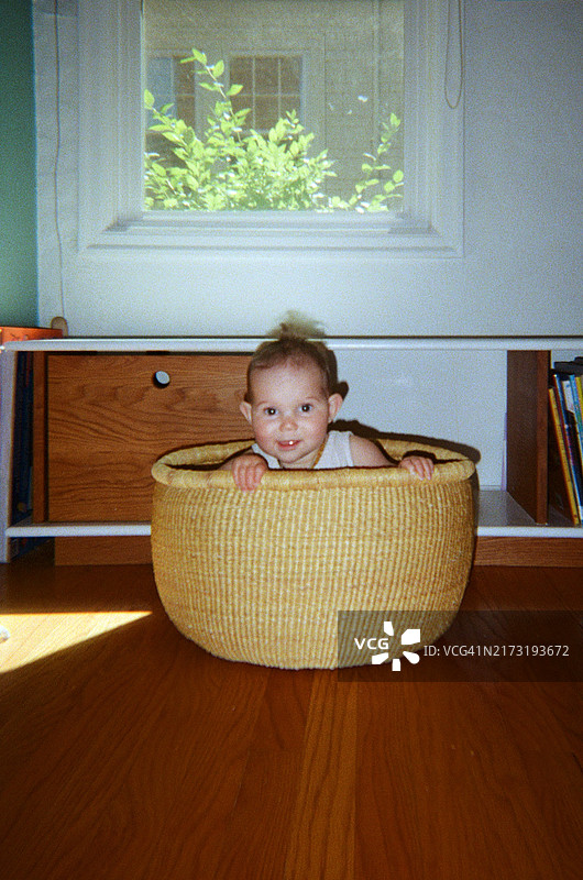 坐在家里篮子里对着镜头微笑的可爱婴儿图片素材