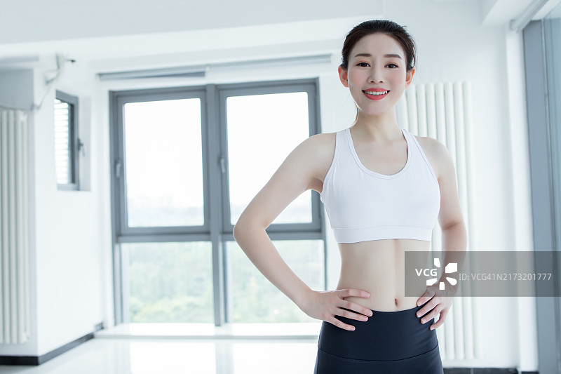 身穿黑色运动服、运动文胸和莱卡裤的运动女性，双手叉腰的正面照图片素材