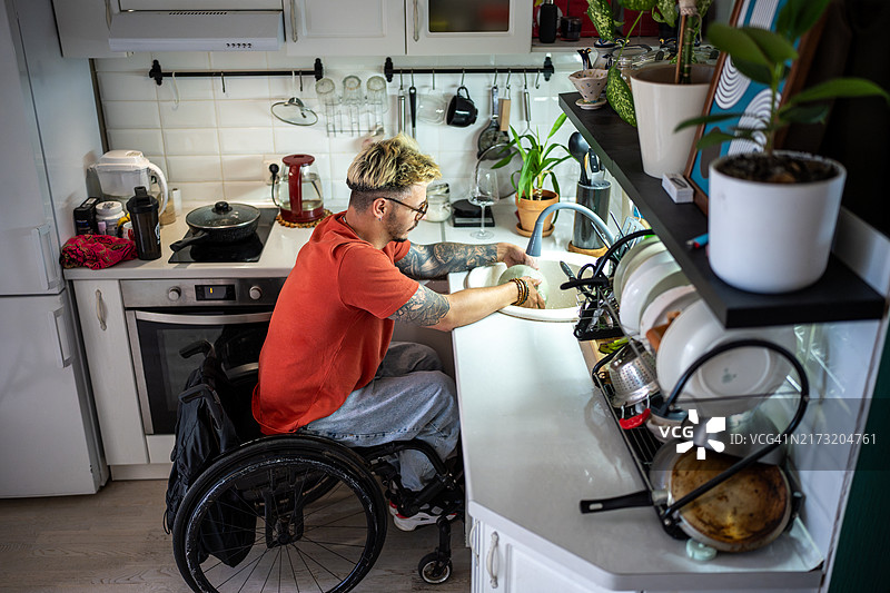 专注的男人坐在轮椅上在厨房的水槽前洗碗图片素材