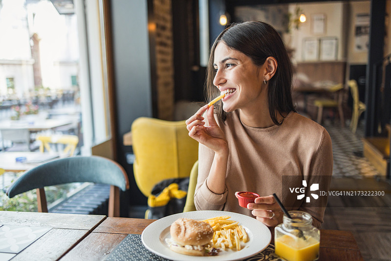 女人在舒适的咖啡馆里吃汉堡和薯条图片素材