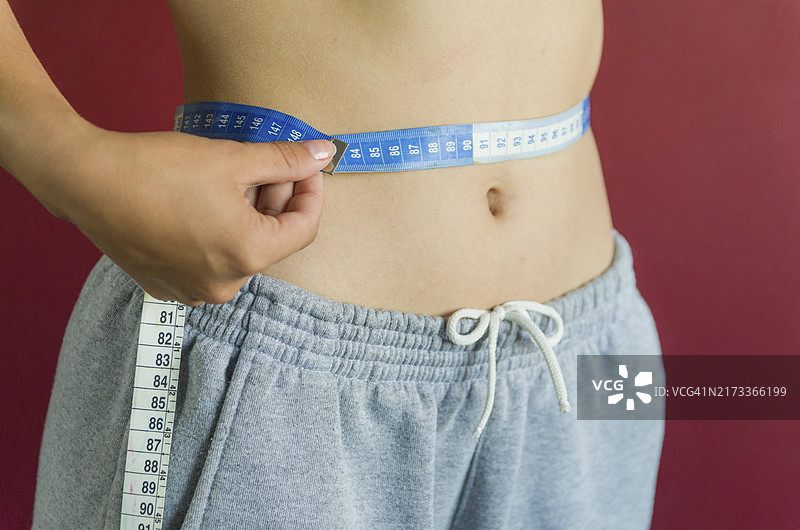 用卷尺测量纤细腰围的苗条年轻女人图片素材