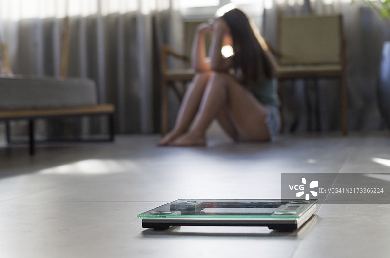 减肥失败的概念：前景是体重秤，背景是沮丧的女人图片素材