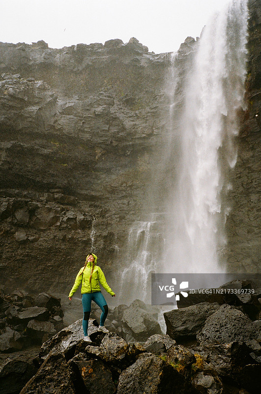 身穿绿色夹克的快乐女人在法罗群岛欣赏壮丽的瀑布（胶片相机拍摄）图片素材