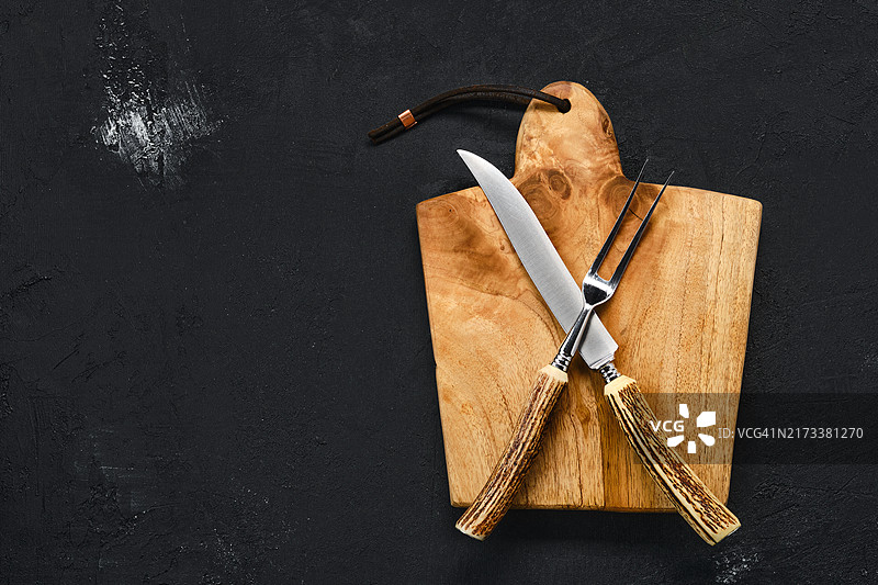 俯视角度：黑色背景上的木制砧板、牛排刀和叉子图片素材