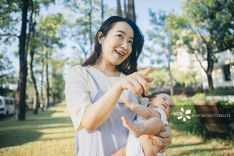 一位亚洲母亲在公园里抱着她的宝宝，享受着宁静的亲子时光。母亲温柔地抱着孩子，二人都放松而满足，在新鲜的空气中享受着与大自然的亲密时刻。图片素材