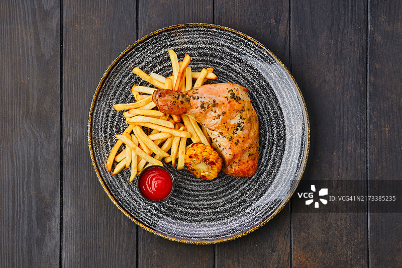 烤鸡腿配炸薯条、烤玉米和番茄酱在深色木桌上的顶视图图片素材