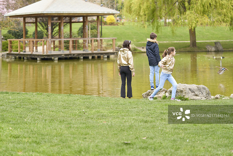 三个男孩站在公园湖岸边看着远处建筑的背影图片素材