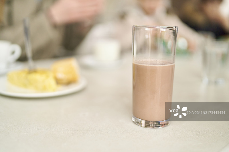 玻璃杯中的巧克力饮料，背景是模糊的食物盘子图片素材