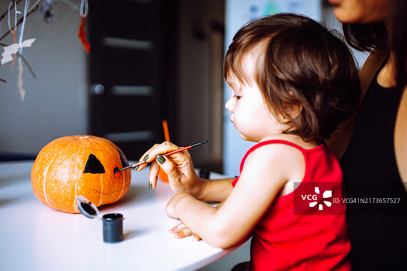 一位女士和她可爱的幼儿女儿用橙色南瓜创作万圣节作品图片素材