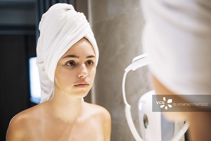 一位年轻女性在浴室镜子前，洗澡后裹着白色毛巾，准备开始新的一天。图片素材