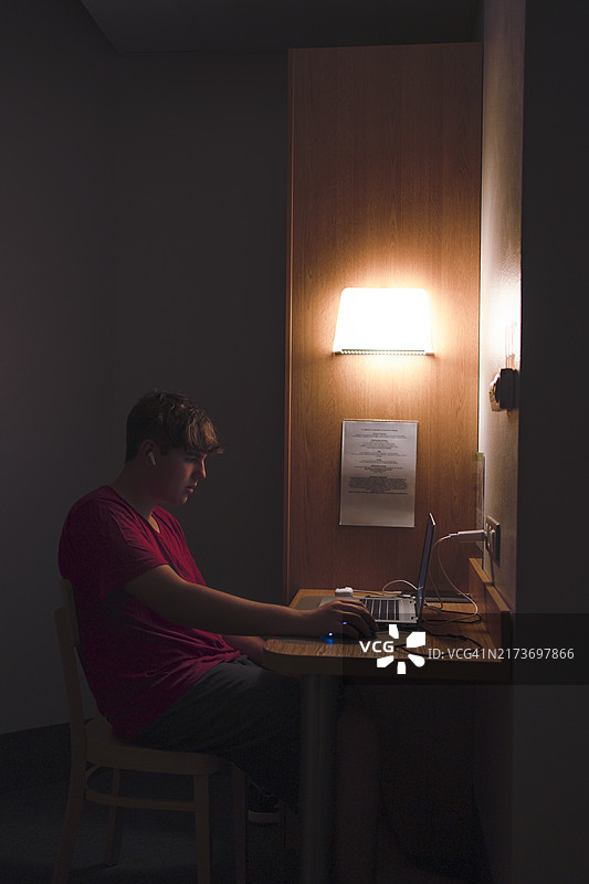青少年在昏暗的酒店房间里使用笔记本电脑图片素材