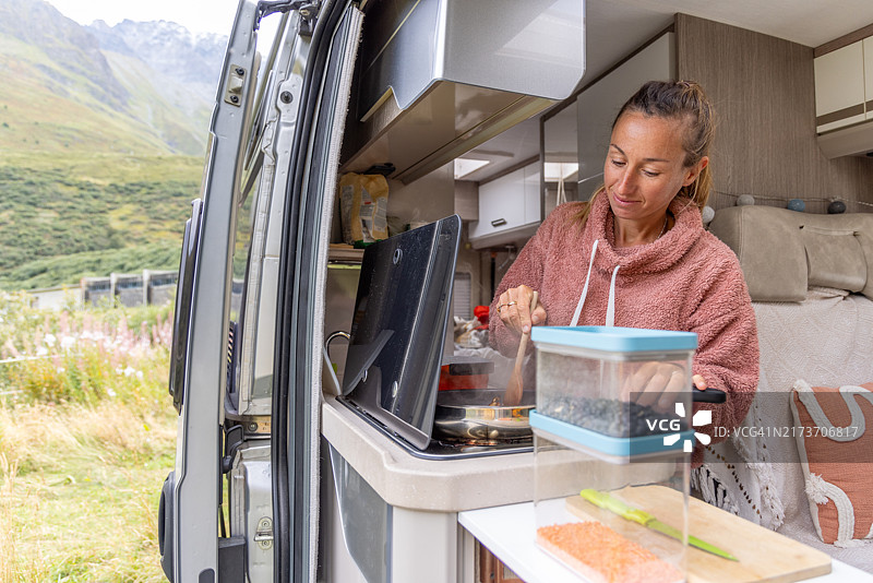 在露营车厨房里搅拌食物的微笑女人图片素材