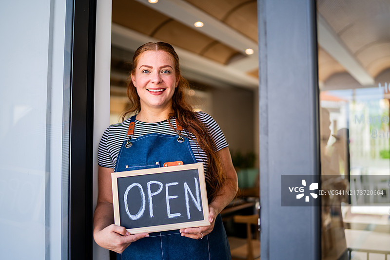 一位成熟的女性在咖啡店里举着写有“开放”的标志图片素材