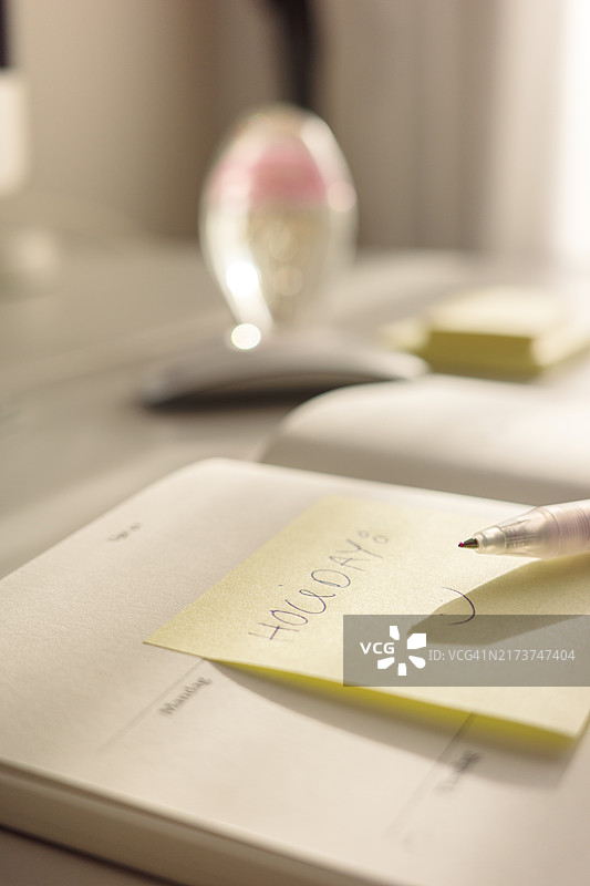 桌子上的日历上有一张黄色便签和一支笔，背景模糊。图片素材