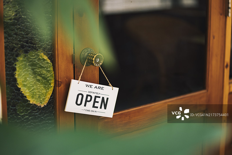 “开放”标志挂在门上，表示咖啡馆现在营业。标志轻轻摇摆，欢迎顾客走进来，咖啡馆开始了新的一天。图片素材