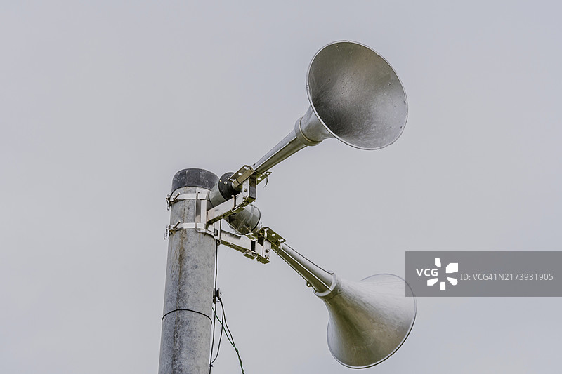 安装在金属杆顶部的用于紧急警告的大型金属扬声器，背景是灰色天空图片素材