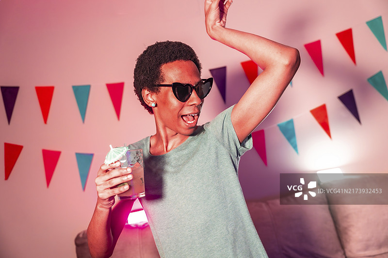 在霓虹灯照亮的公寓里，拉丁男人跳舞和喝鸡尾酒图片素材