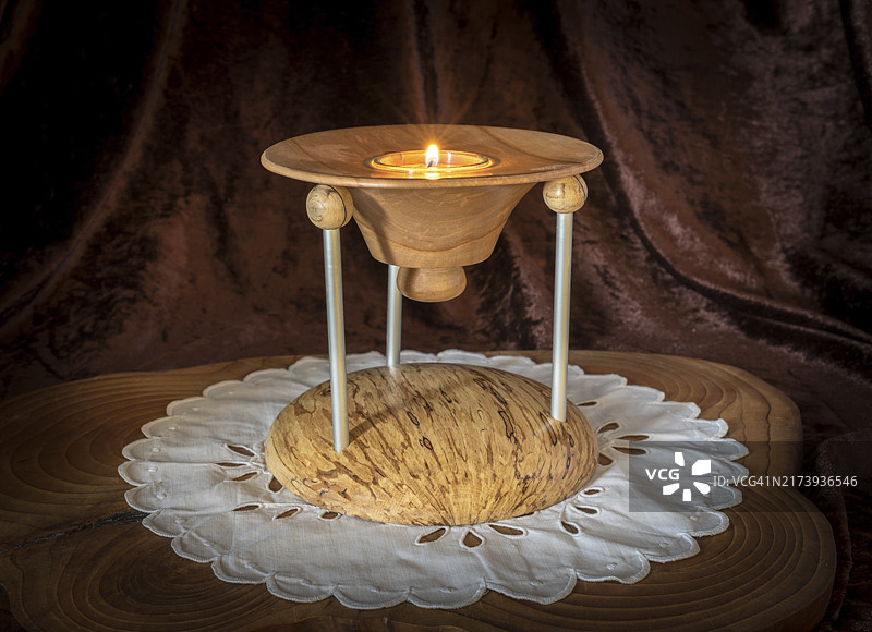 多节木制烛台，燃烧的蜡烛立于深色木板上，背景为棕色图片素材