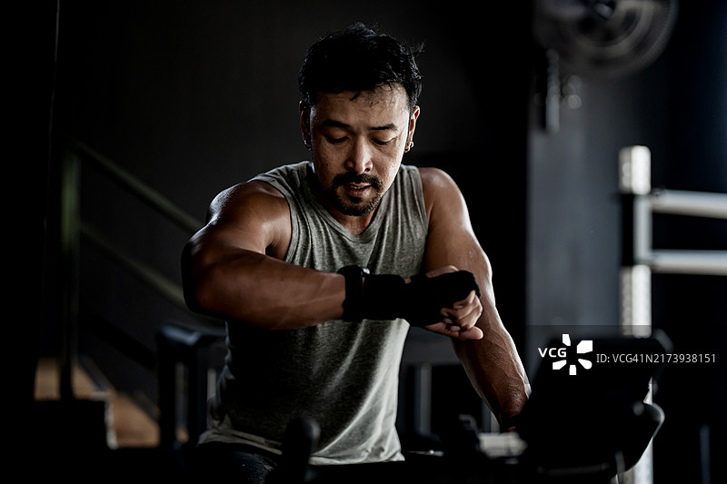 在健身房进行有氧运动的男运动员：身穿运动服的年轻亚洲男性在坐式自行车上查看智能手表图片素材