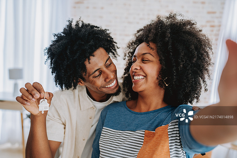 幸福的夫妇购买新房，拿着钥匙用智能手机自拍图片素材