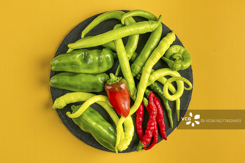 黄色背景下的圆形盘子上盛放的各种绿色和红色辣椒图片素材