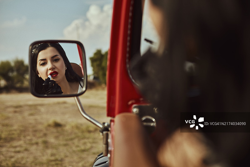 复古风格的女人在敞篷越野车的后视镜上涂口红图片素材
