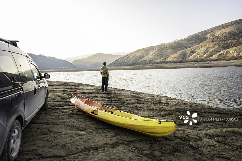 皮划艇之旅：沉思的男人看着汽车附近的湖泊，探险旅游图片素材