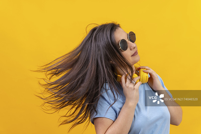黄色背景下戴耳机挥舞头发的女人工作室肖像照图片素材