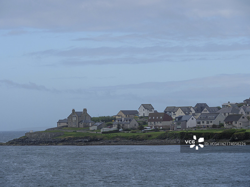 英国苏格兰设得兰群岛勒威克沿海城镇，石头房屋和绿草，平静的海面，多云的天空图片素材