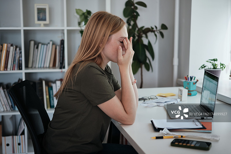 在家用笔记本电脑工作的疲惫自由职业女性揉眼睛，远程工作者感到疲倦，眼睛疲劳和视力问题图片素材