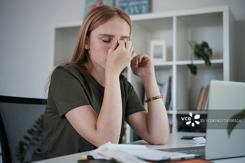 在家用笔记本电脑工作的疲惫自由职业女性揉眼睛，远程工作者感到疲倦，眼睛疲劳和视力问题图片素材