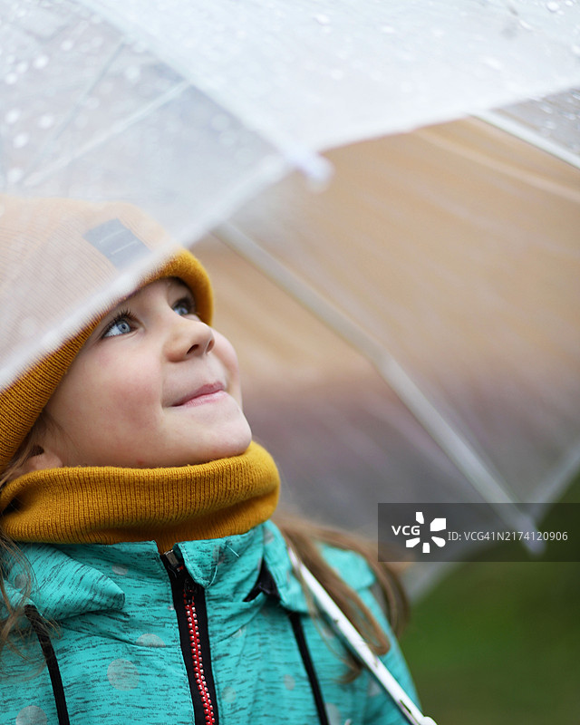 一个6岁的女孩在一把透明的伞下，笑着看着从伞上流下的雨滴图片素材