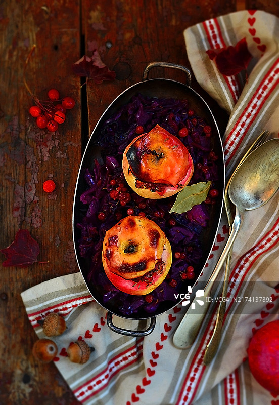 炖红甘蓝与填充苹果放在金属复古碗中，背景为木质桌面。图片素材