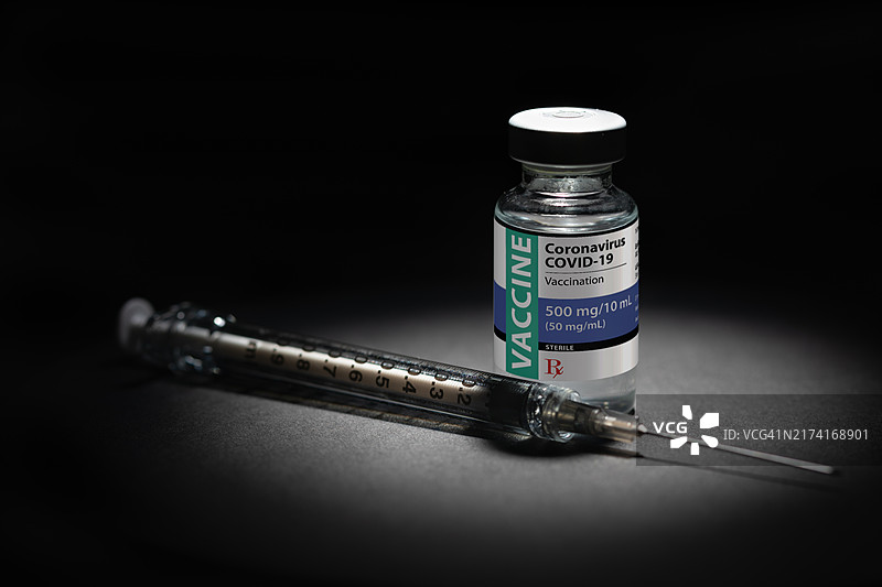 深色背景上聚光灯照射下的注射器针头和新冠COVID-19疫苗瓶图片素材