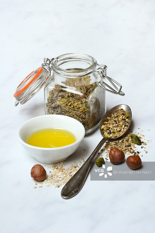 阿拉伯调料Dukkah，装在玻璃容器和勺子里，还有坚果和小碗橄榄油图片素材