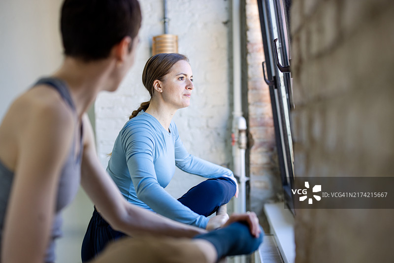 两位年轻女性在舞蹈工作室的横杆上做腿部拉伸。图片素材